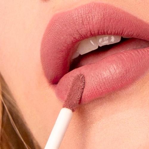 Eine Person, die mit einem Applikator rosa Lippenstift oder Lipgloss aufträgt. Nahaufnahme von Mund und Make-up-Werkzeug.