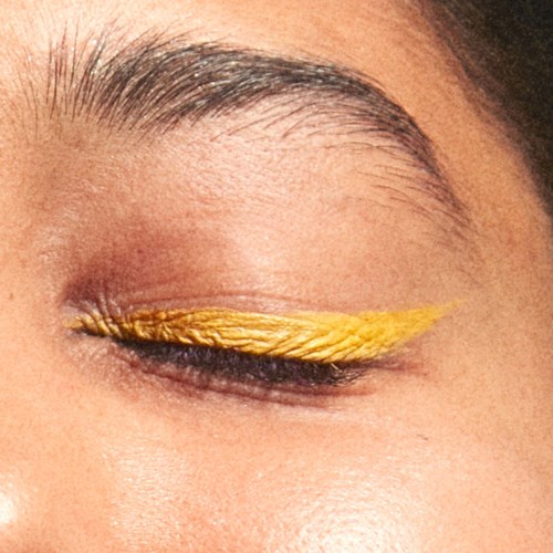 Et lukket øje med gul vinge-eyeliner og naturlige bryn.