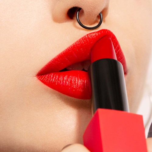 Close-up of lips with bright red lipstick, a nose ring, and a lipstick tube touching the lips.