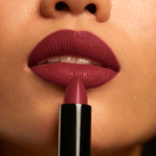 Close-up of lips with lipstick being applied, showing smooth, dark pink lips and part of a face.