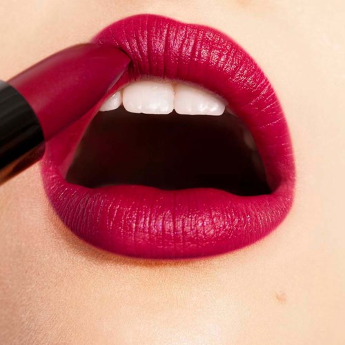 Red lipstick being applied to lips, with part of lipstick visible. Lips are slightly open, showing teeth.