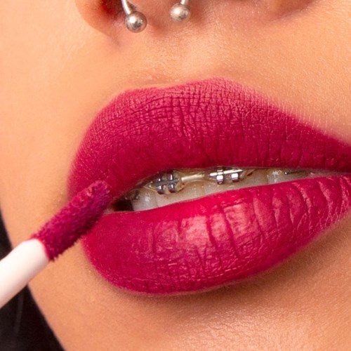 Nahaufnahme von Lippen mit Spangen, beim Auftragen von pinkem Lippenstift und Lipgloss.