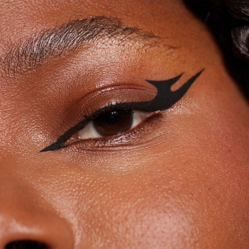 Henkilön silmässä on raju musta eyeliner, jossa on terävät, rohkeat linjat ja liekkimäinen design. Iho on sileä ja hehkuva.