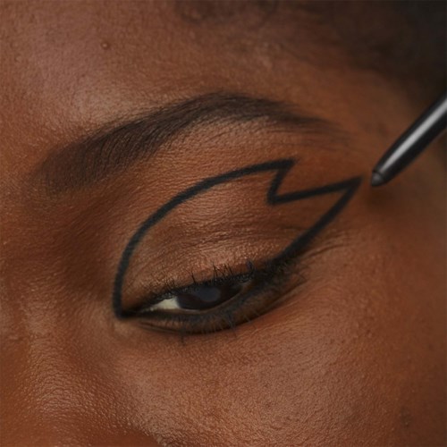 A person is drawing a lightning bolt on their eyelid with a black pen or pencil.