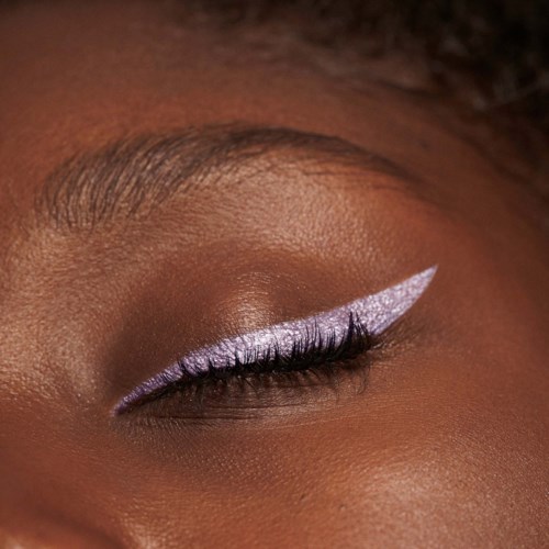 An eye with makeup, including purple eyeshadow and a striking white eyeliner with a sharp wing.