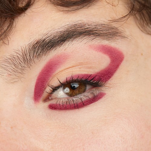 A person has bold red makeup on the eyelid, eyebrow, and lower lash line, creating a striking look.