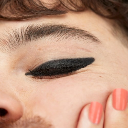 Et nærbillede af en person med sort eyeliner, der viser deres øje og del af ansigtet med en hånd.