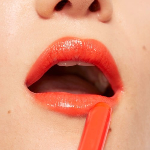 Närbild på en person som lägger orange läppstift på läpparna.