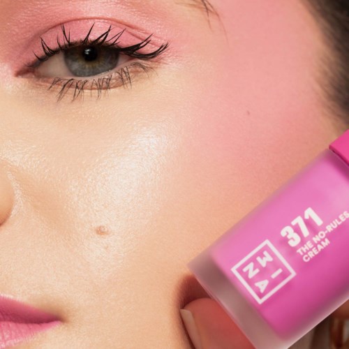 Nainen pitäää pinkkiä pulloa, jossa lukee '37.1 The No Rules Cream', lähellä kasvojaan.