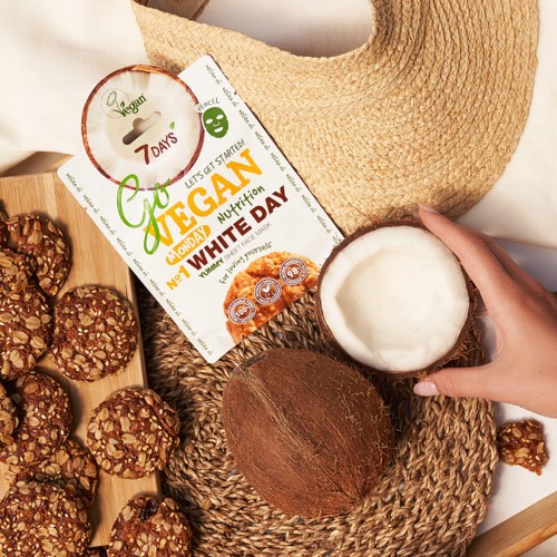 En kokosnøtt, kjeks, en sommerskjerm og en vegansk ernæringsplanflyer på et vevd teppe. Noen holder i kokosnøtten.