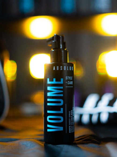 A black bottle with blue text stands on a surface, background of bright yellow lights creating a blurred glow.