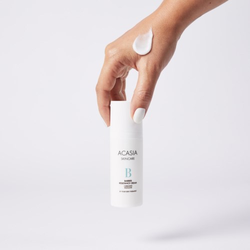 En hånd med hvid neglelak holder en hvid flaske mærket ACASIA SKINCARE, med creme på fingeren.