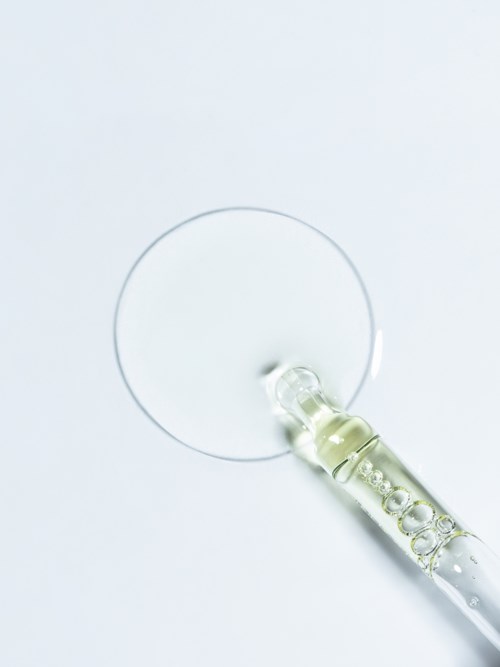 En klar pipette som slipper væske på en hvit overflate, med et rundt merket der væsken lander.