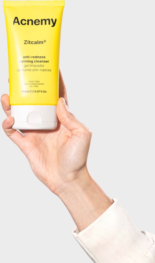 A hand holds a yellow tube labeled 'Acne My', with text about calming and redness. Clear background.