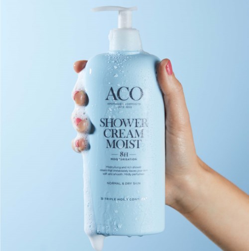 Blaue Duschcremeflasche mit Schaum auf Hand, beschriftet 'ACO Shower Cream Moist 8H', für normale und trockene Haut.