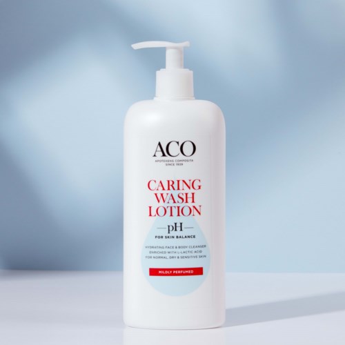 Vit flaska med pump, märkt 'ACQ Caring Wash Lotion' för ansikte och kropp, lätt parfymerad, på blå bakgrund.