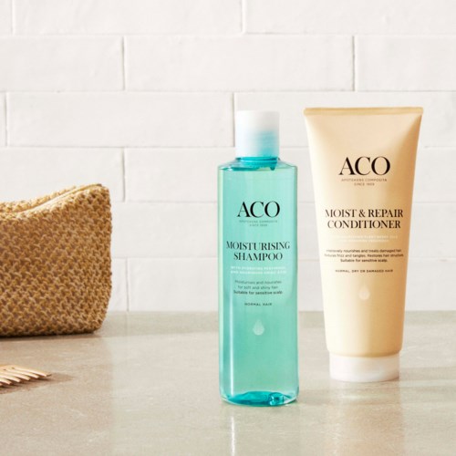 The image shows two hair care products, a shampoo and a conditioner, on a countertop with a white wall background.