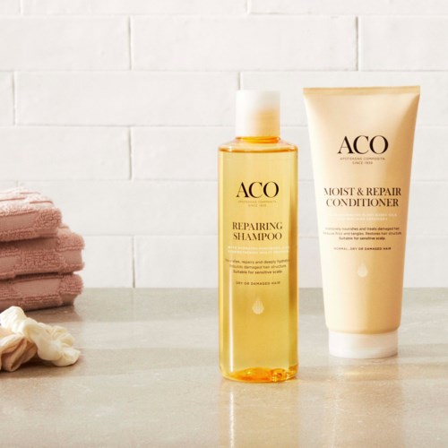 Two bottles of hair care products, one shampoo and one conditioner, with pink towels and a white wall background.