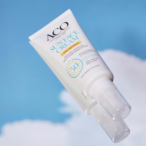 En vit tub med solkräm med SPF 50, lutad mot en blå himmel och moln i bakgrunden.
