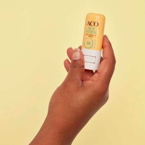 Eine Hand hält einen gelben und weißen Lippenbalsam mit dem Namen ACO.