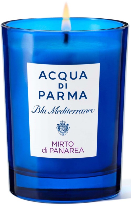 Een blauwe kaars in een glas met lont en vlam. De kaars heeft een wit label met tekst en een wapenschild.