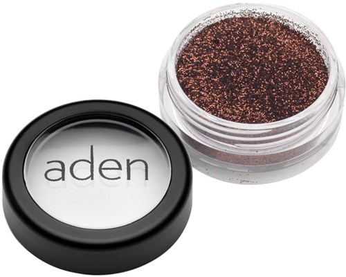 A compact with a clear lid showing dark glittery eyeshadow inside. The compact has the word "aden" on the lid.