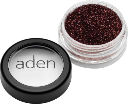 Ein kleiner Behälter mit dunkelrotem Glitzer neben einem schwarzen Behälter mit der Aufschrift 'aden' und durchsichtigem Deckel.