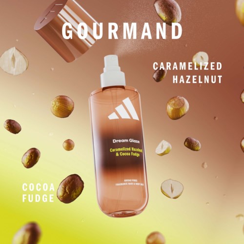 En spray med smak av karamelliserad hasselnöt och kakao fudge, omgiven av spridda hasselnötter och bitar. Bakgrunden har varma färger. GOURMAND-tekst högst upp.
