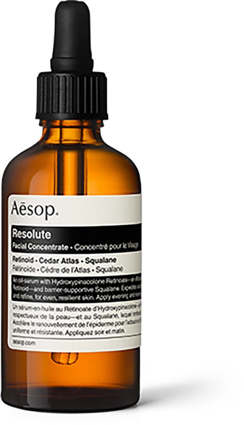 A small amber glass bottle with a black dropper cap, labeled with product details for skin care.