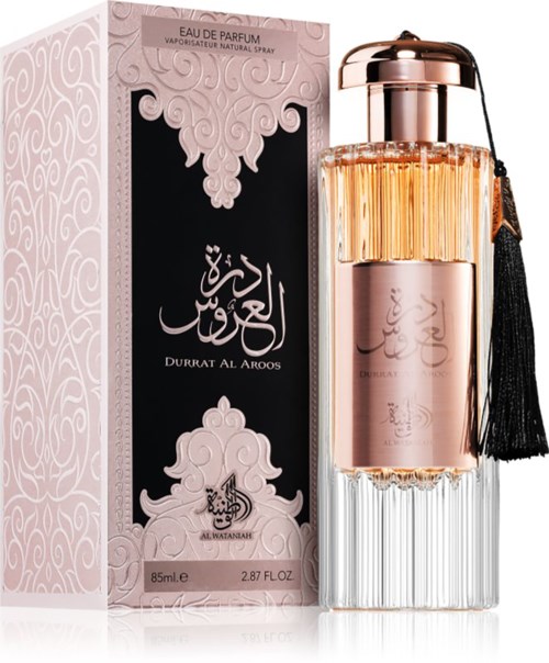Een roze parfumfles met een zwarte kwast, naast een sierlijk roze en zwarte doos met Arabisch schrift.