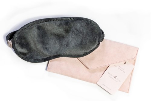 En mörk sovmask med mjuk, sammetsliknande yta bredvid ett rosa kuvert och ett litet kort.