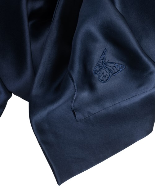 En mörkblå tygbit med en broderad fjärilslogotyp, ser mjuk och glänsande ut, troligen en del av ett klädesplagg.