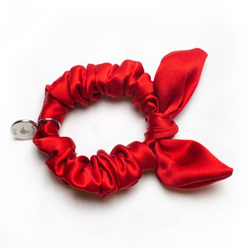 En röd tygscrunchie med en stor rosett och ett litet smycke fäst.