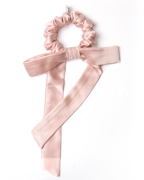 En ljusrosa scrunchie med stor rosett på en vit bakgrund.