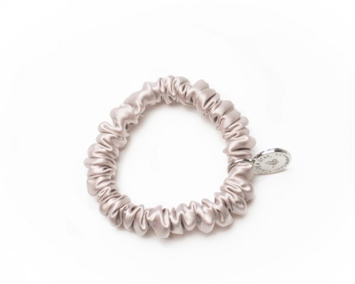 A light-colored satin scrunchie with a small oval tag attached.
