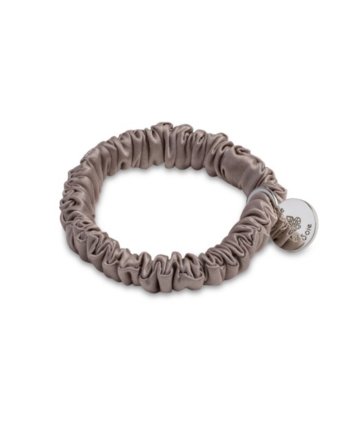 A beige fabric scrunchie with a small charm attached, shaped in a circle.