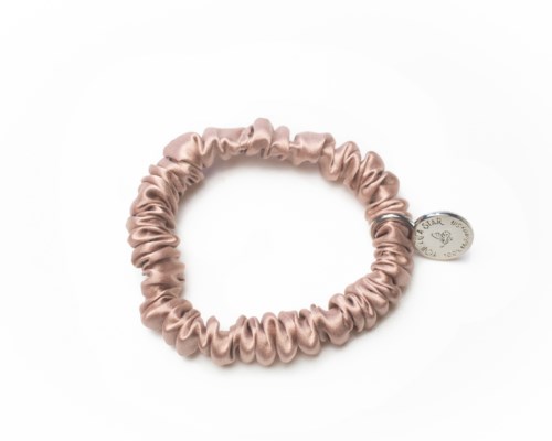 En rosa scrunchie med en liten silverhake som ser ut som ett mynt.