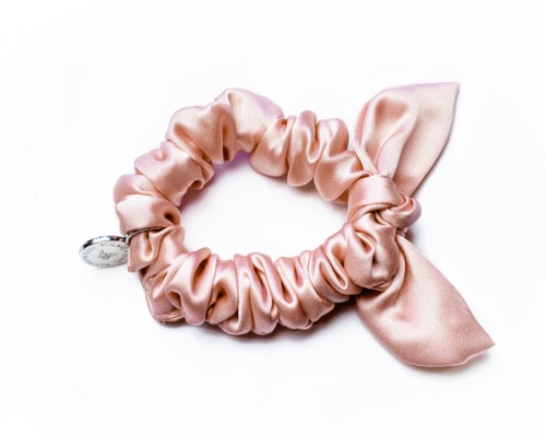En rosa satin scrunchie med rosett och en liten charm fastsatt.