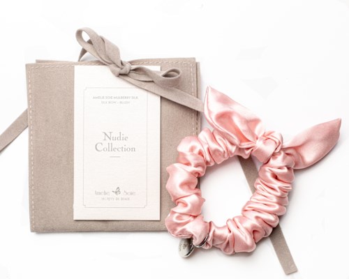 En beige låda med ett rosa satin-tysle och en liten tagg, på vit bakgrund.
