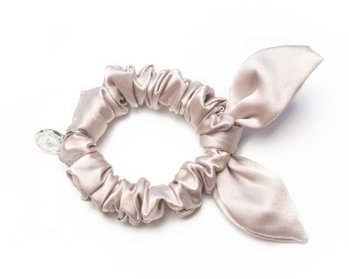 En ljus satin scrunchie med rosett på sidan. Den används för att knyta hår.