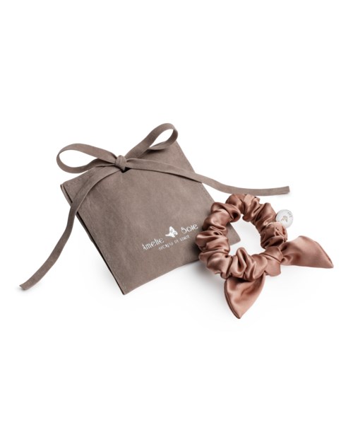 Eine beige Tasche und ein passender Satin-Haarband liegen auf einem weißen Hintergrund.