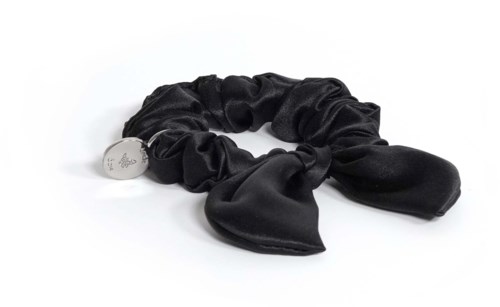 Ein schwarzes Satin-Haarband mit Schleife, verbunden mit einem kleinen silbernen Anhänger, auf einer weißen Oberfläche.