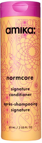 En rosa og gul flaske merket 'Amika: Normcore Signature Conditioner' med blomster- og geometriske mønstre.