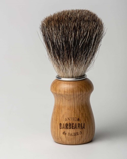 Een scheerkwast met houten handvat en dichte borstels. Het handvat heeft de tekst "Antiga Barbearia de Bairro" gegraveerd.