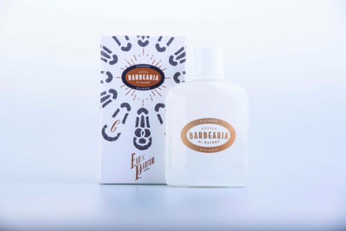Een witte fles met een label en een doos, beide met zwarte patronen en bruine tekst. Ze lijken verzorgings- of schoonheidsproducten.