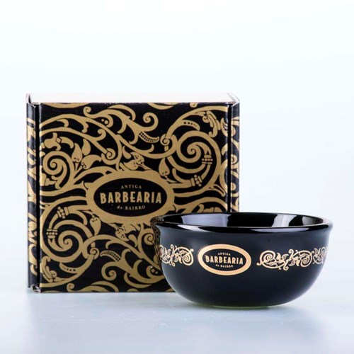 Een zwarte kom met gouden versieringen en een bijpassende doos met ingewikkelde gouden patronen en het label 'Antiga Barbearia'.