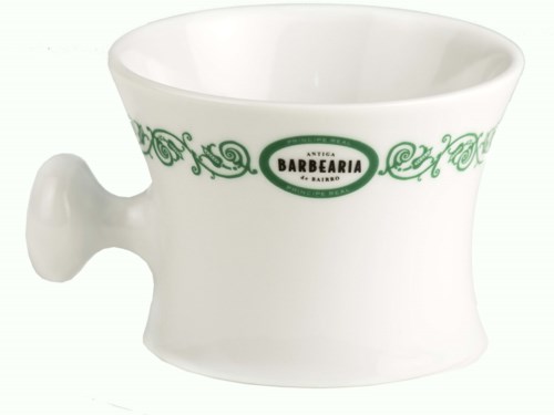 En vit mugg med gröna dekorativa mönster och en logotyp som säger "Antica Barbearia".