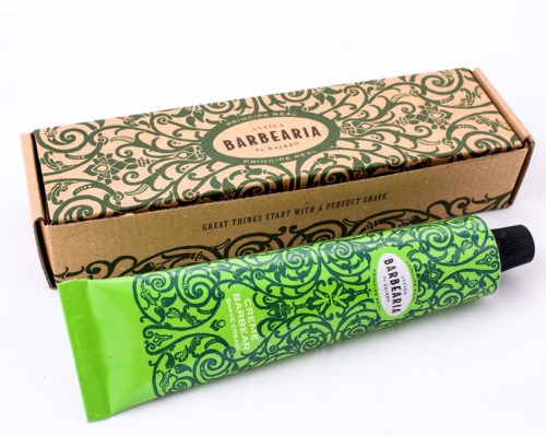 Een groene tube baardbalsem met zwarte dop en een decoratieve doos met de merknaam "Barbearia" en ingewikkelde ontwerpen.