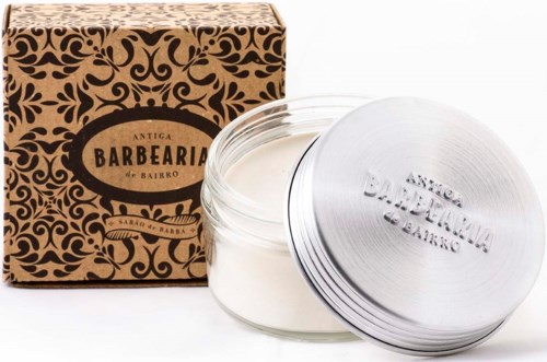Een pot met witte crème, metalen deksel en een decoratieve bruine doos met een label. Het label zegt 'Antiga Barbearia do Bairro.'
