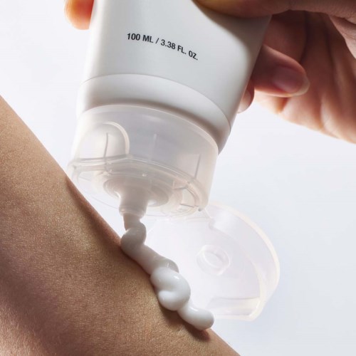 Eine Hand drückt weißen Lotion aus einem Tuben auf den Arm. Die Tube ist mit 100 ML oder 3,38 FL OZ beschriftet.